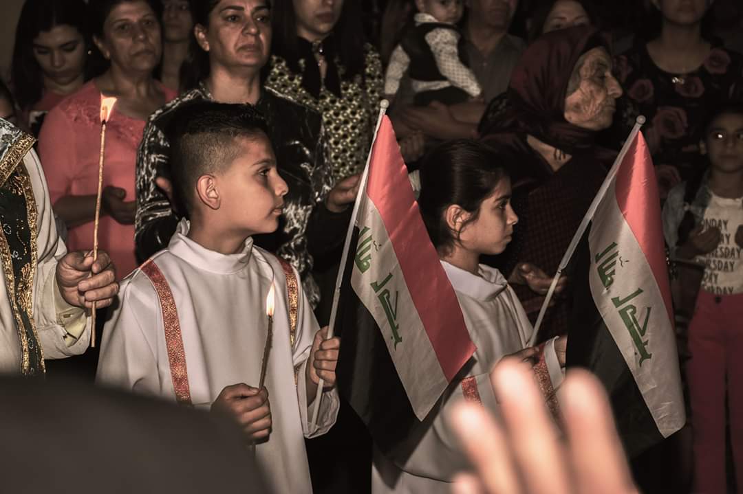 En la Iglesia de los Santos Behnam y Sarah en Qaraqosh, la ciudad cristiana más grande de Irak, los católicos se reunieron para rezar por la paz en su país, con los servidores del altar llevando banderas iraquíes para la ocasión.