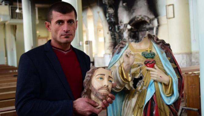 Cristiano en la iglesia de Mar Addai, en el pueblo iraquí de Karemlesh, mostrando la estatua del Sagrado Corazón, decapitada por el Daesh. (ACN) Cristiano en la iglesia de Mar Addai, en el pueblo iraquí de Karemlesh, mostrando la estatua del Sagrado Corazón, decapitada por el Daesh. (ACN)